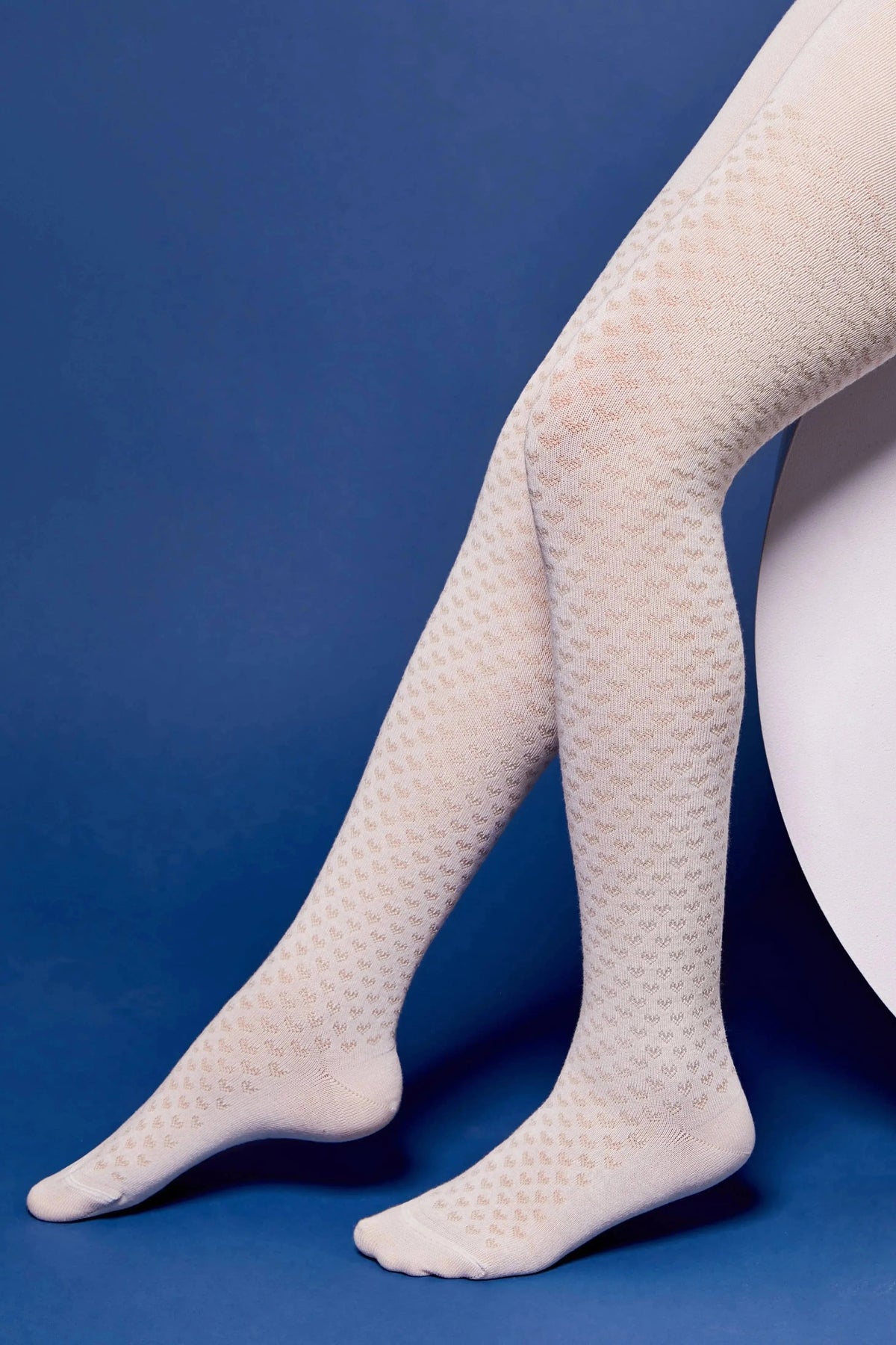 Patterned cream-colored tights worn on a model's legs against a solid blue background.