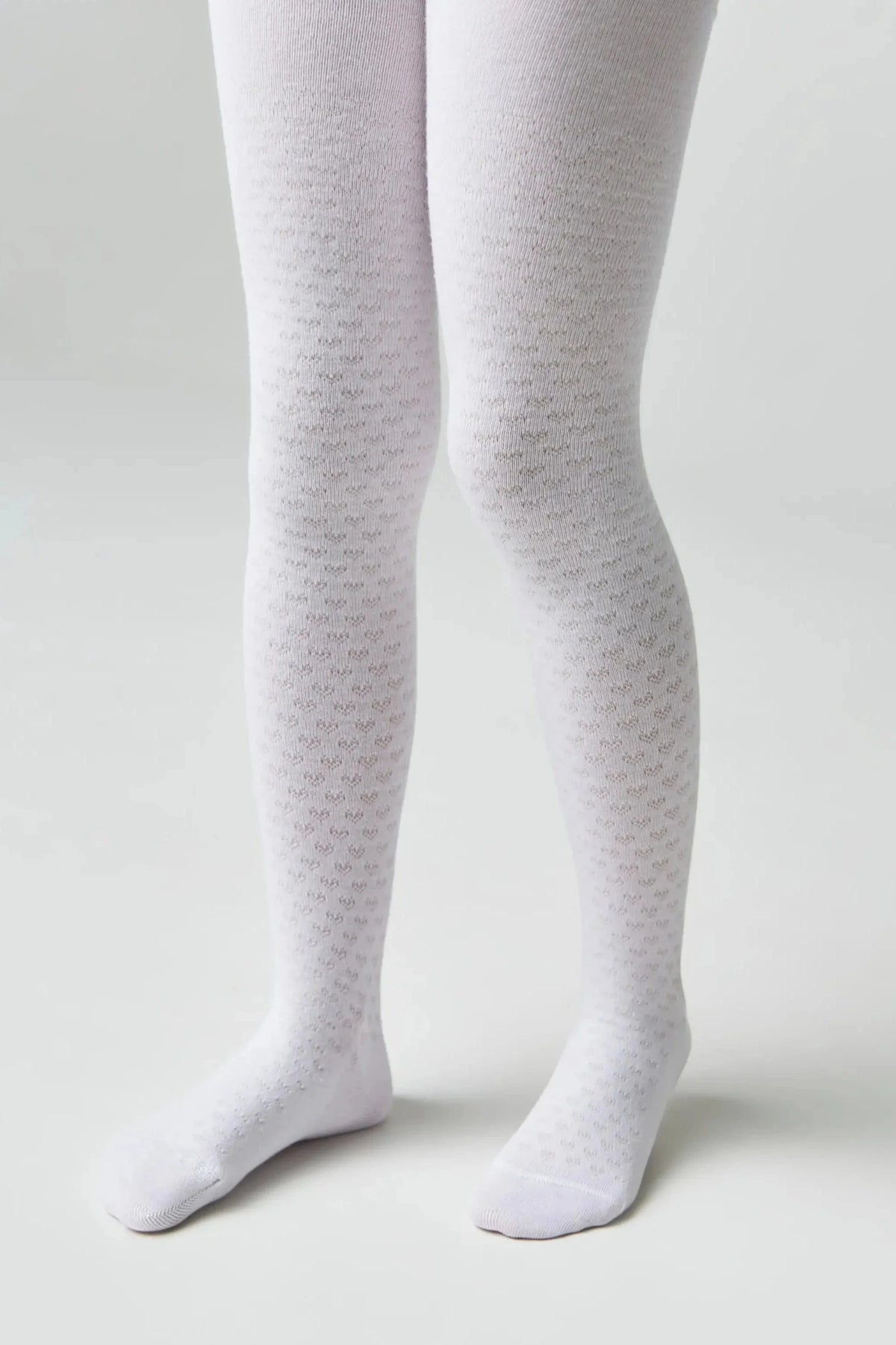 White patterned tights with a textured micro-heart print worn on a child's legs against a solid light gray background.