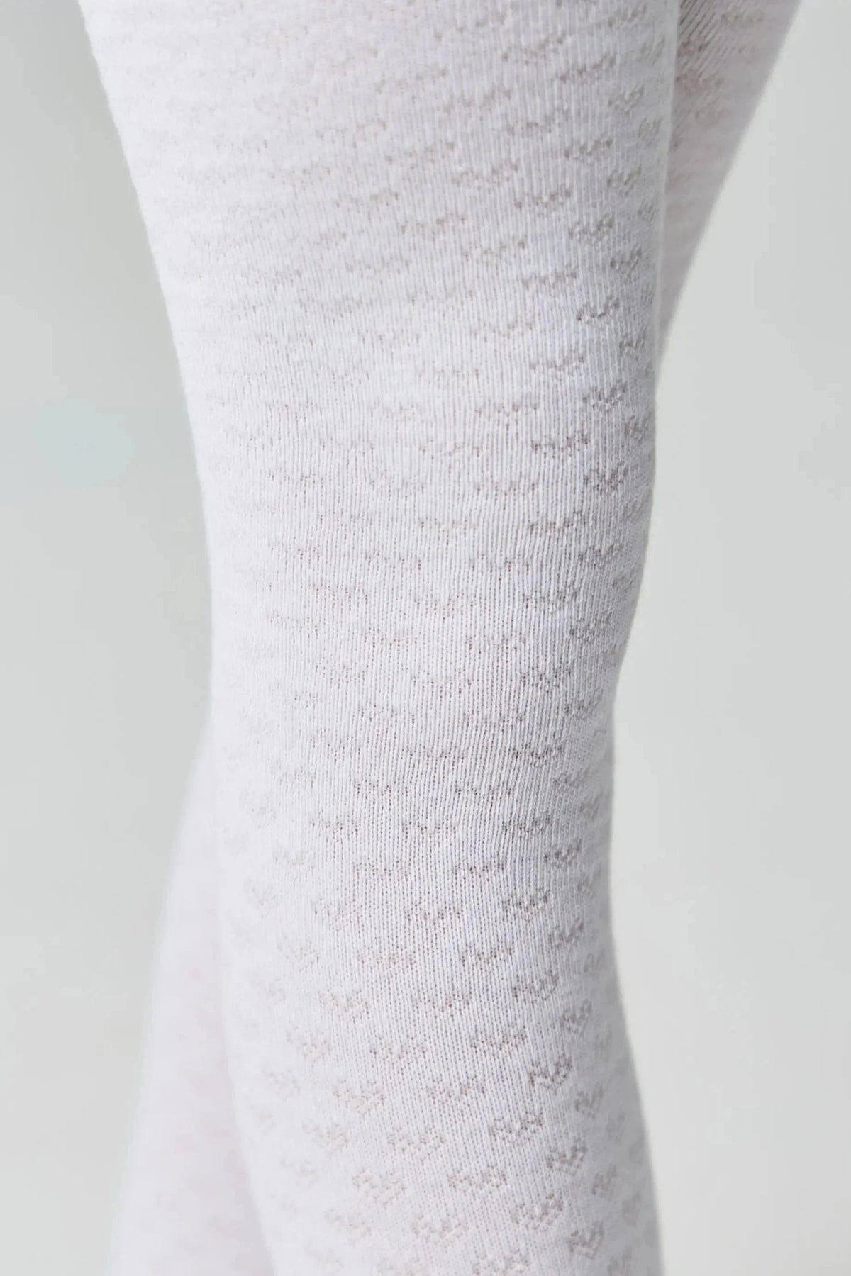 Close-up view of white opaque tights featuring a subtle, repeating heart pattern texture against a plain light gray background.