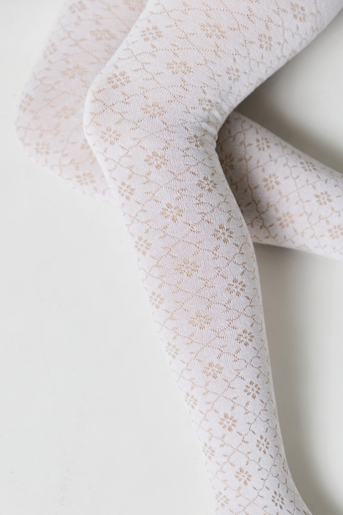 White tights featuring a delicate, repeating floral diamond pattern in light brown against a plain, off-white background.