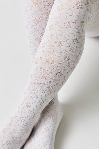 White tights featuring a repeating diamond grid pattern filled with small beige floral or snowflake motifs, worn on crossed legs against a plain background.