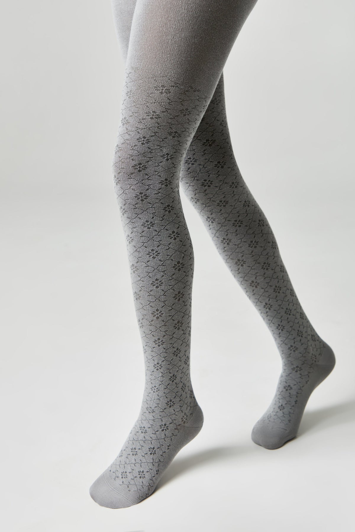A pair of grey tights with a repeating small floral pattern worn on a model against a light grey background.