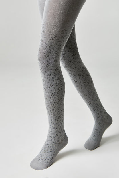 A pair of grey tights with a repeating small floral pattern worn on a model against a light grey background.