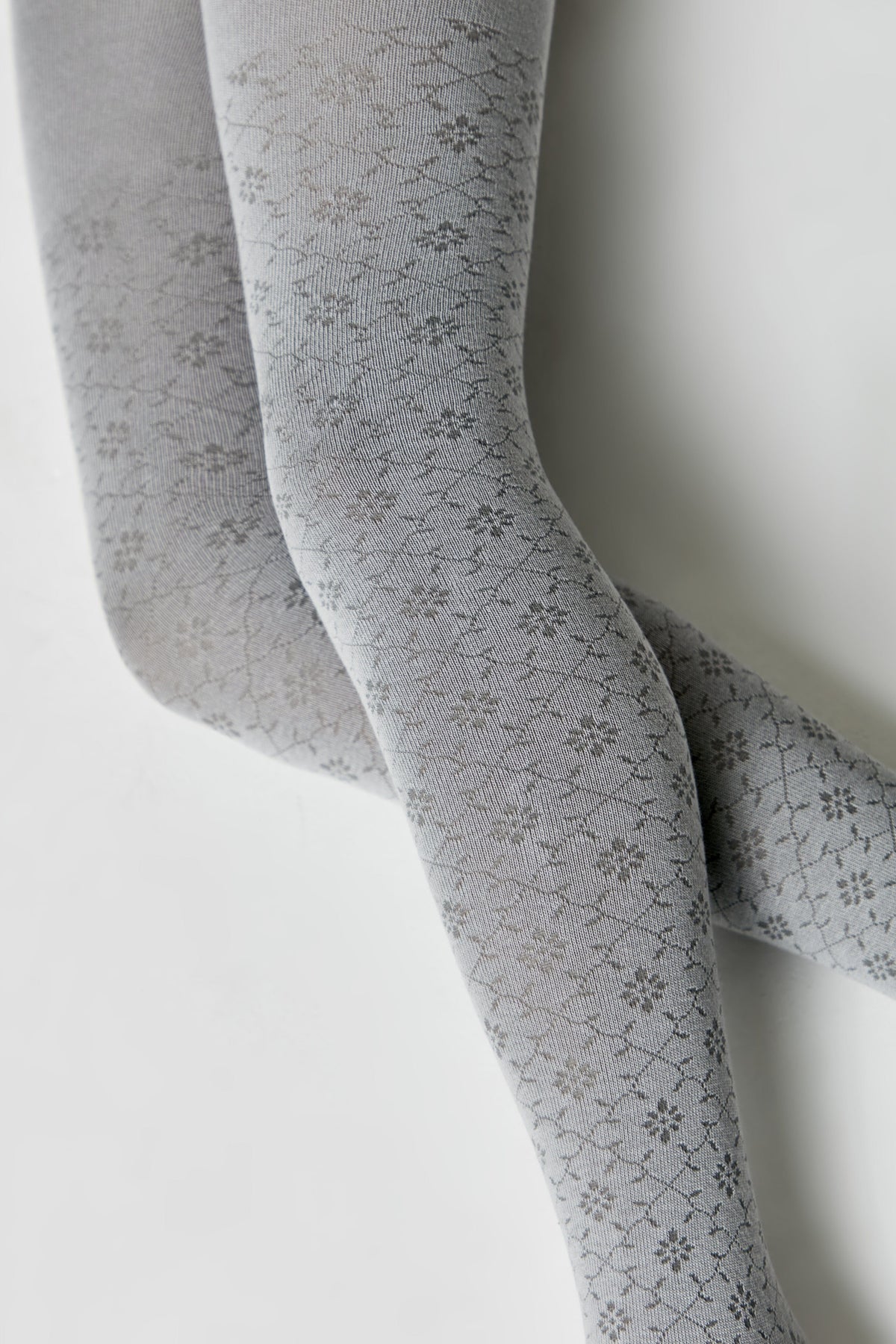 A pair of grey tights featuring a repeating floral and diamond-shaped pattern against a solid, light grey background.