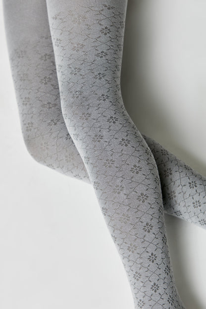 A pair of grey tights featuring a repeating floral and diamond-shaped pattern against a solid, light grey background.