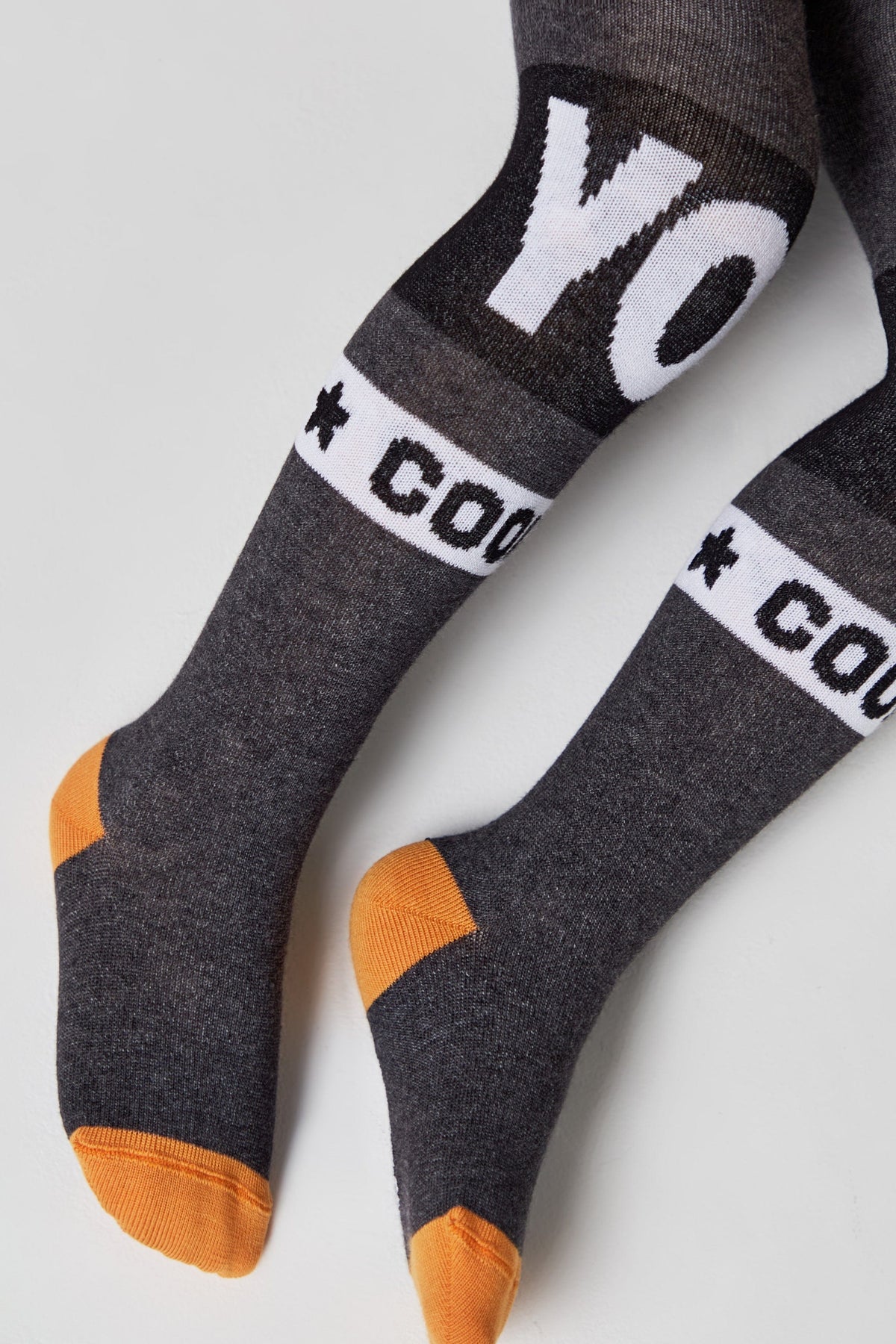 A pair of children's grey knit tights featuring white band details with the text YO and COOL with star accents, finished with solid orange heels and toes.