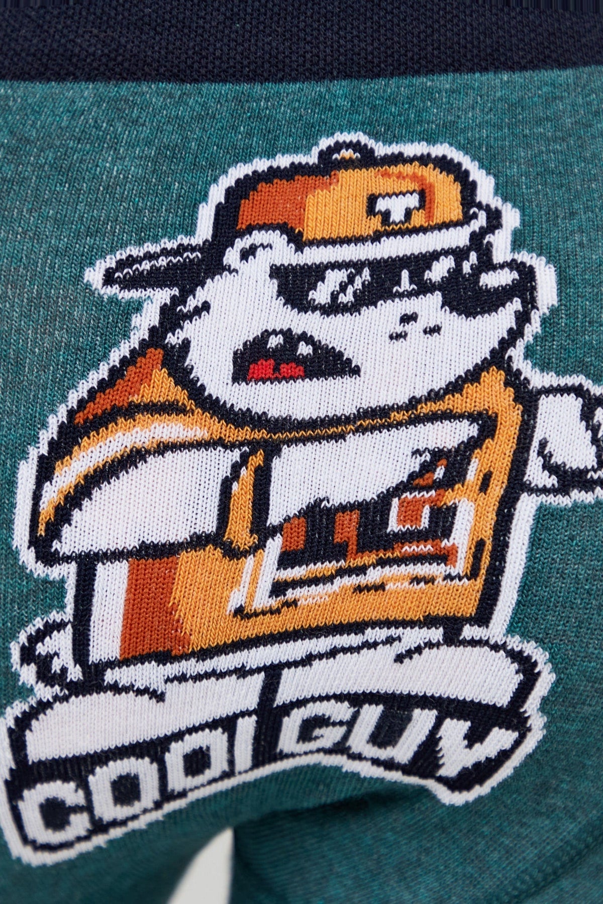 A close-up of a teal knit fabric featuring a cartoon bulldog wearing an orange and white cap and shirt, with the words COOL GUY embroidered in white below the figure.