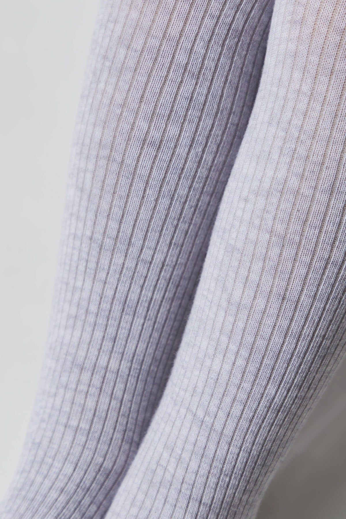 A close-up of two legs wearing light purple, ribbed knit socks against a plain white background.