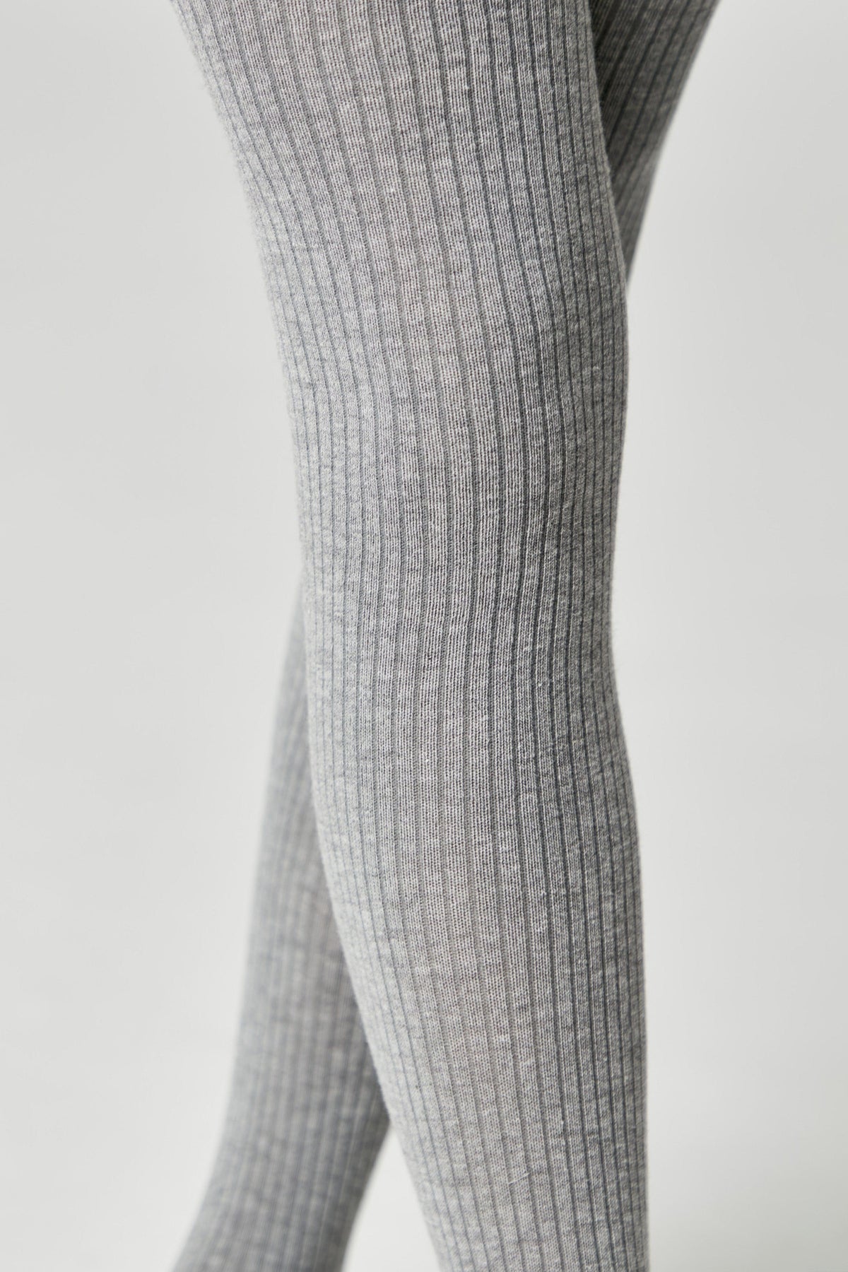 A close-up view of ribbed grey tights worn on a person's legs against a plain light-grey background.
