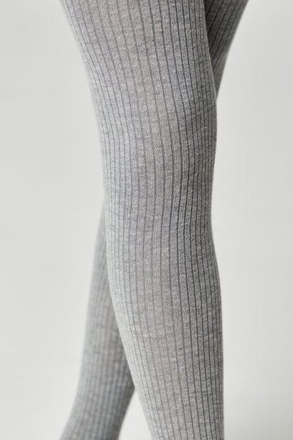 A close-up view of ribbed grey tights worn on a person's legs against a plain light-grey background.