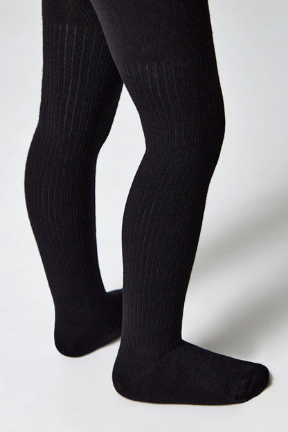 A pair of black ribbed tights worn on a child's legs against a plain light gray background.