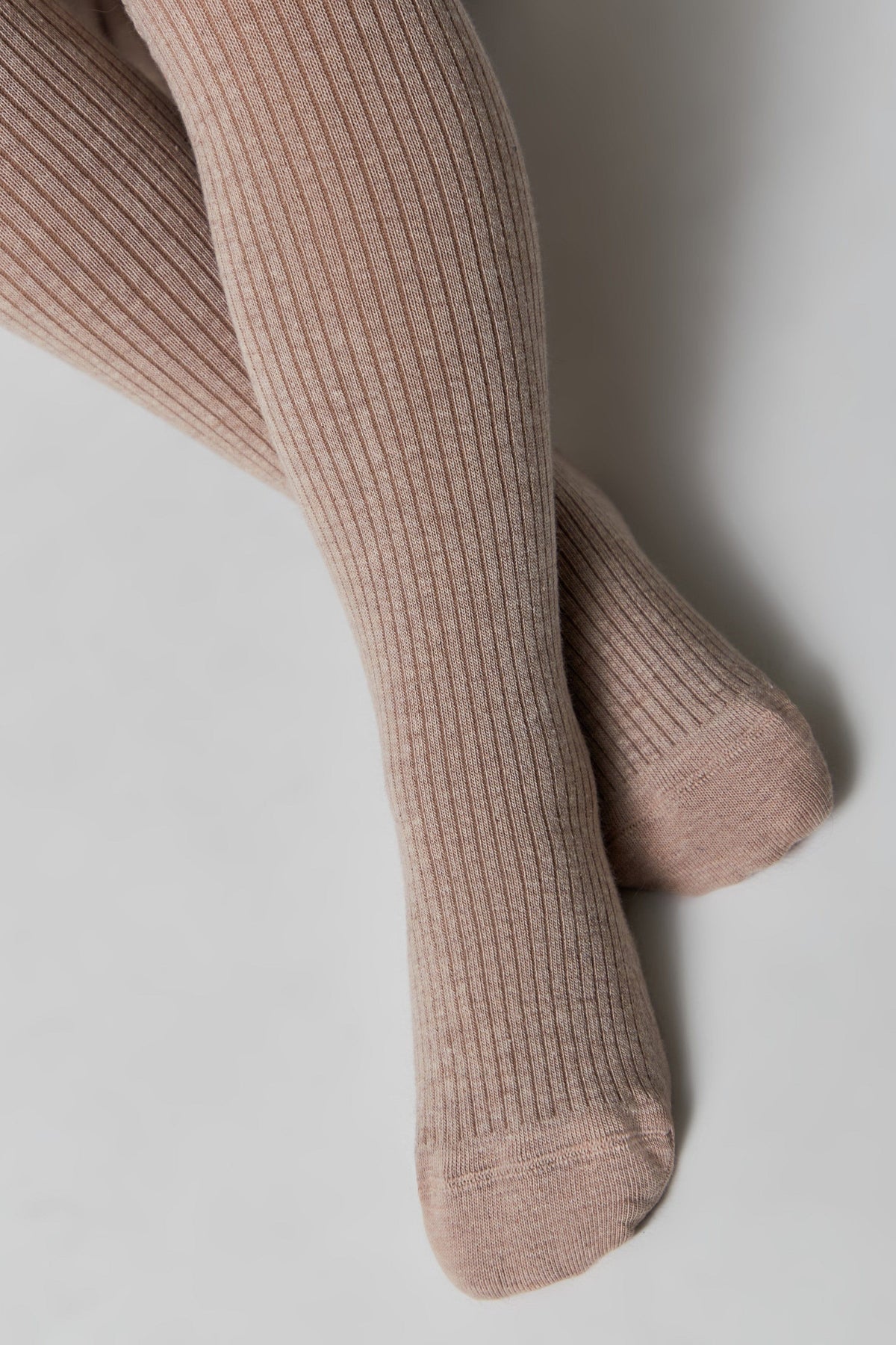 A pair of light tan ribbed knit tights worn on legs, angled against a plain white background.