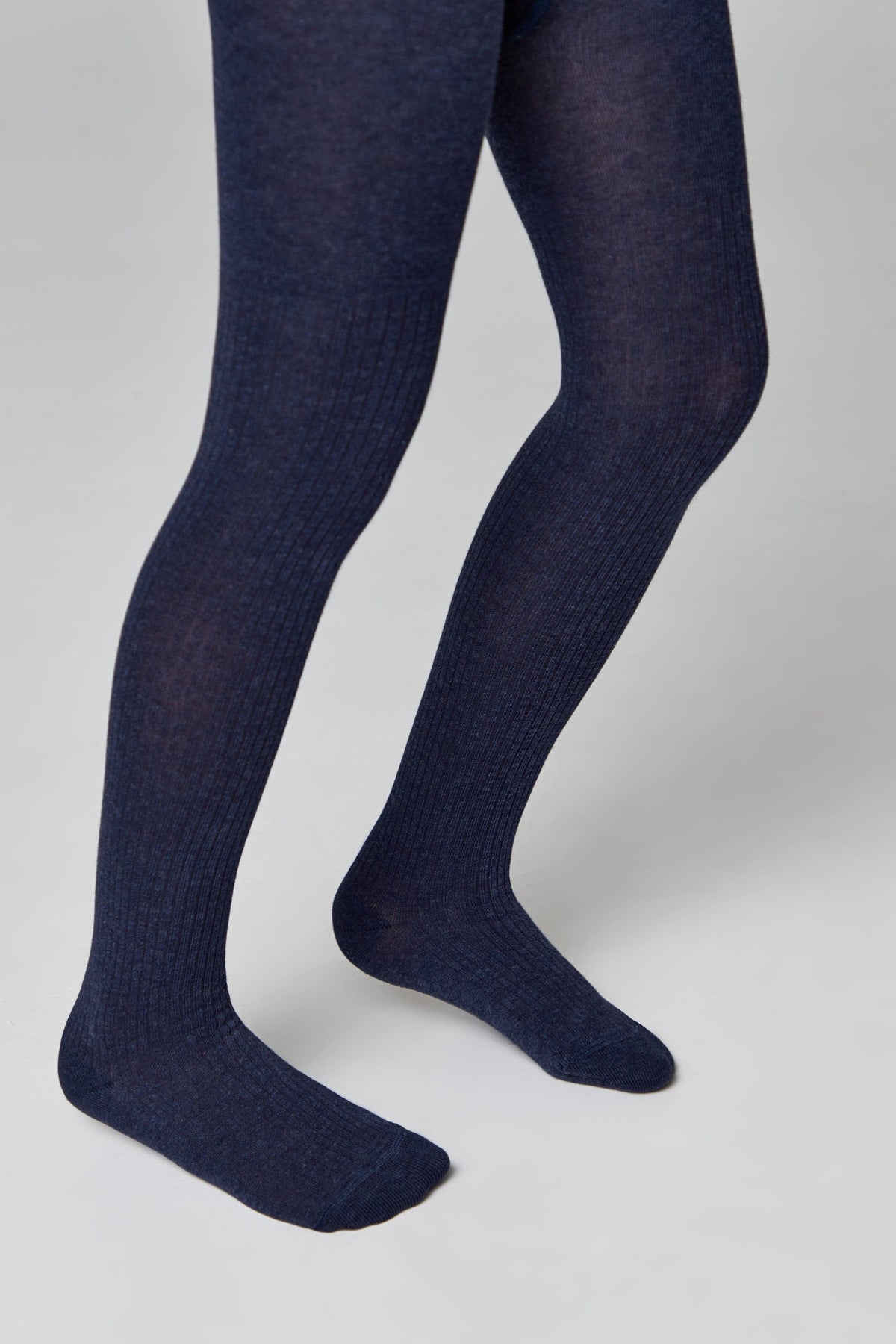 A pair of ribbed dark blue tights are worn on the legs against a plain light gray background.