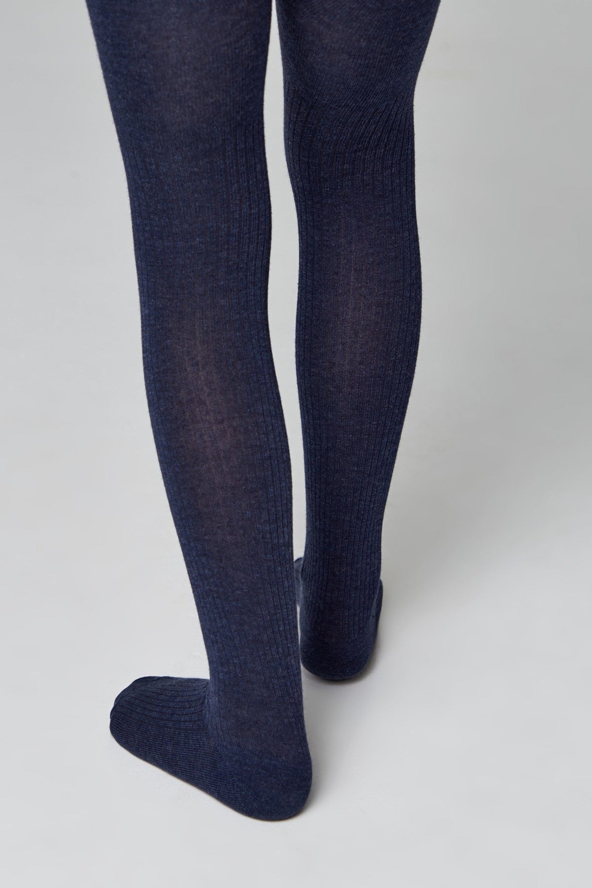 A pair of ribbed, dark navy blue footed tights worn on a person's legs against a plain light grey background.