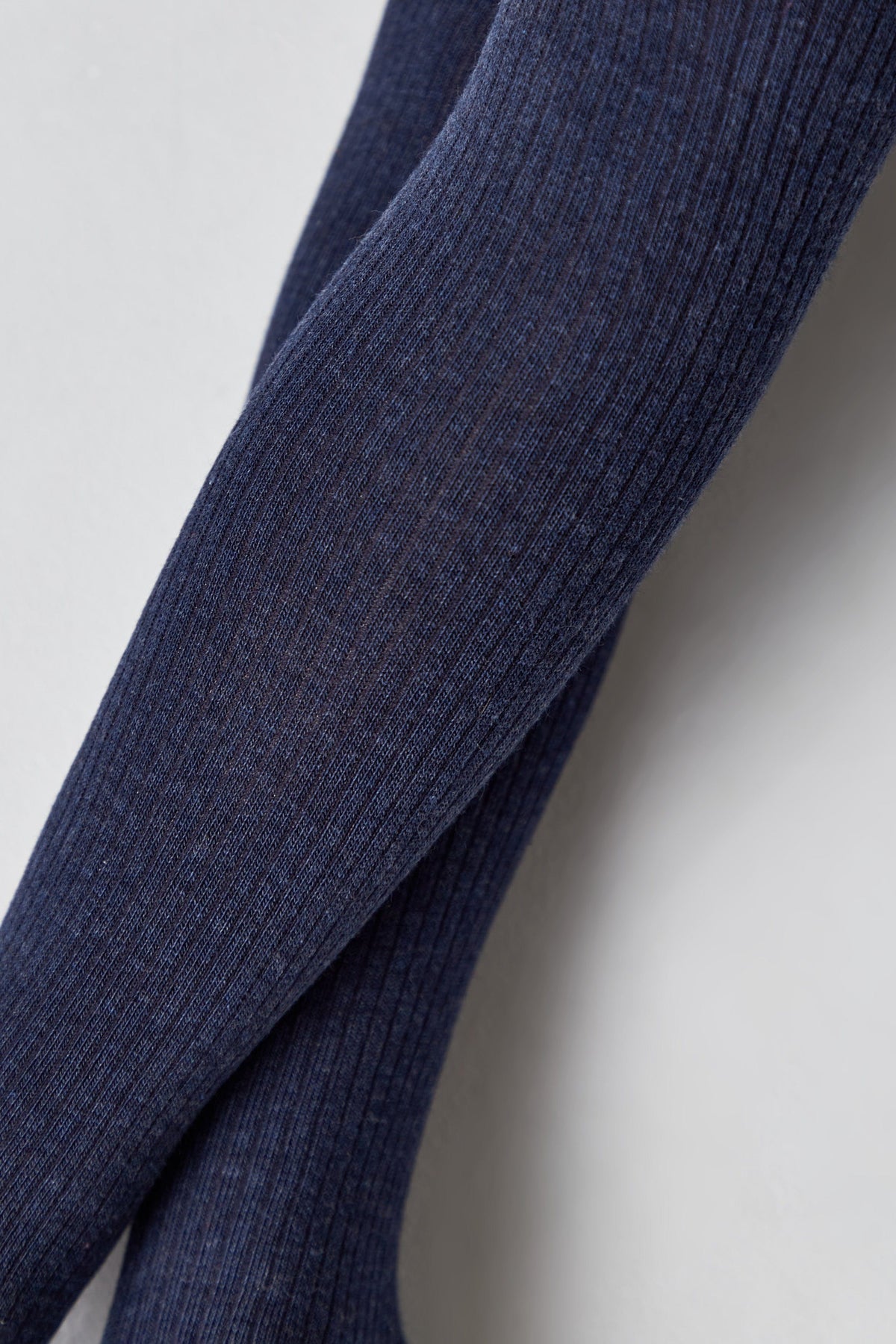 A close-up view of ribbed fabric in a dark blue color, featuring a vertically textured knit pattern.
