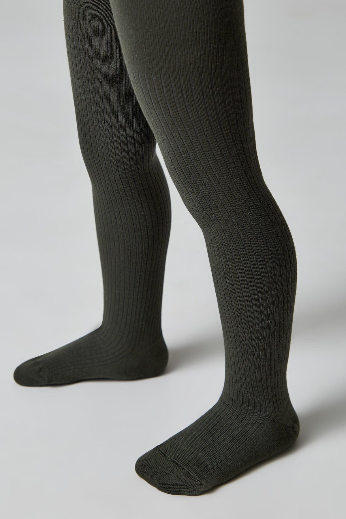 A pair of dark olive green ribbed tights worn on a child's legs against a plain light gray background.