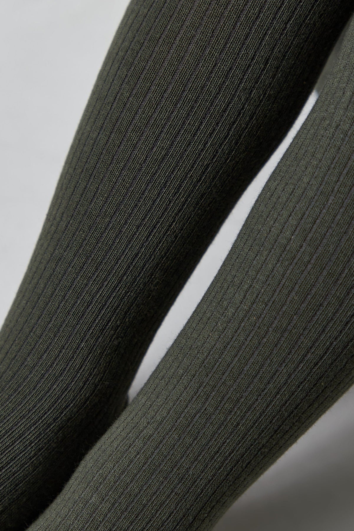 A close-up view of ribbed olive green tights worn on a person's legs against a plain background.