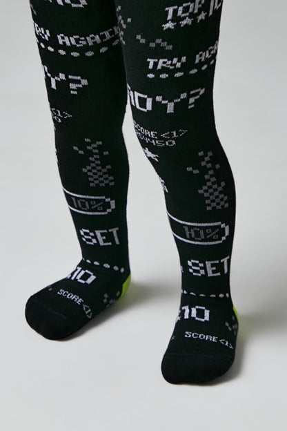 Black tights for children featuring a pixelated, retro video game-inspired pattern in white including text like TRY AGAIN, 10 PERCENT, and SCORE along with battery icons.