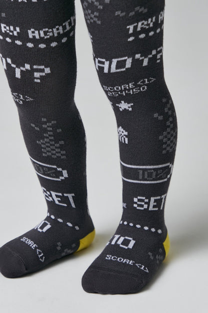 A pair of dark grey knitted tights for children featuring a white 8-bit retro video game pattern with text including "TRY AGAIN", "READY?", "SCORE <1>", and "SET" along with battery icons.