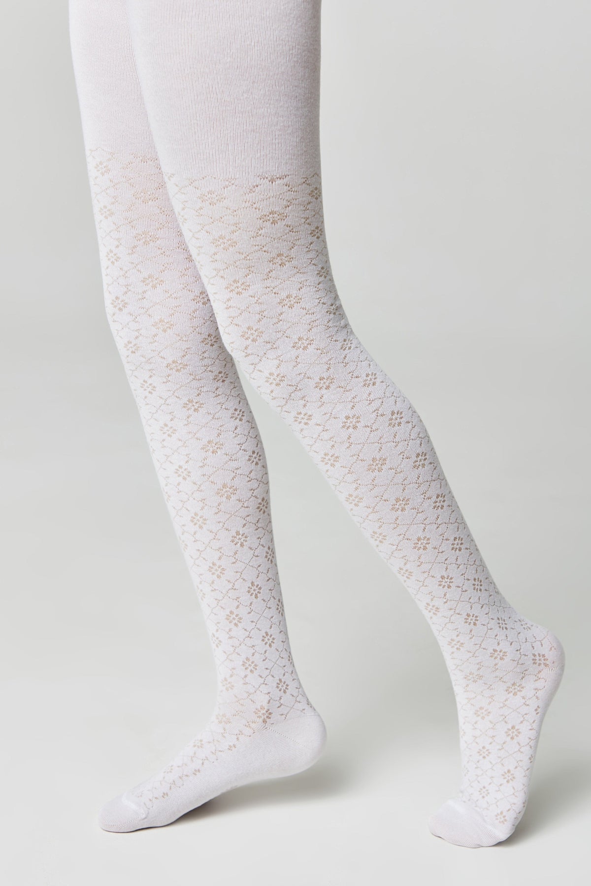 A pair of white tights featuring a delicate floral lace pattern throughout the legs, worn by a person against a plain light gray background.
