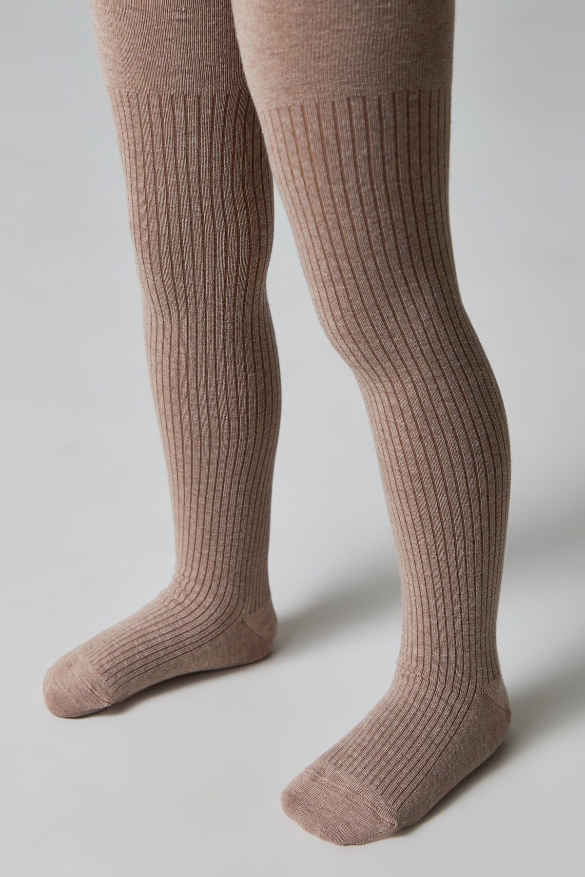 Ribbed tights in a light brown color are worn on a pair of legs against a plain light gray background.
