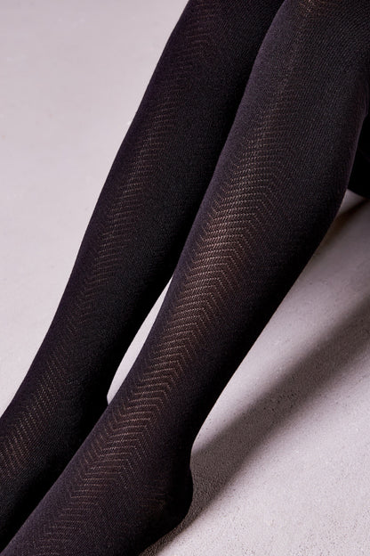 A close-up view of legs wearing black opaque tights featuring a subtle textured herringbone pattern.