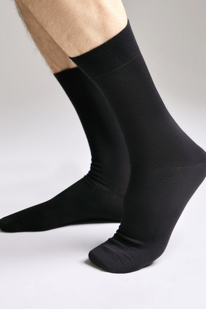 A person wearing plain black crew-length socks against a plain light gray background.
