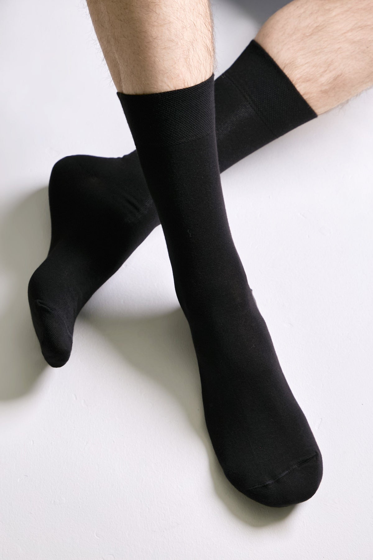 A pair of plain black calf-length socks worn on a person's feet against a white background.