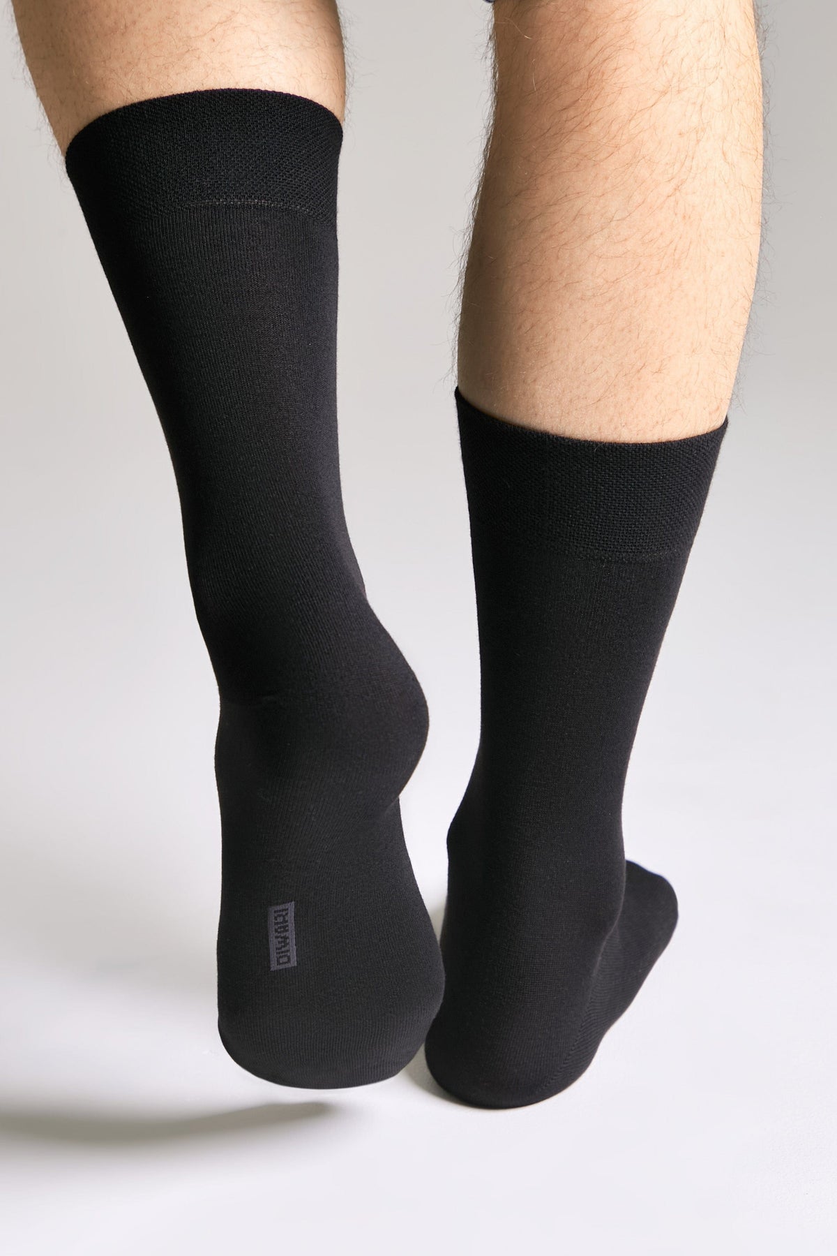 A pair of plain black calf-length socks worn on a person's lower legs against a light grey background.
