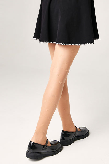 Sheer tan pantyhose featuring a subtle, repeating small bow pattern, worn with a black flared skirt and black patent leather mary jane shoes.