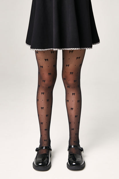 Black sheer pantyhose patterned with small black bows worn with a black flared skirt and shiny black Mary Jane shoes.