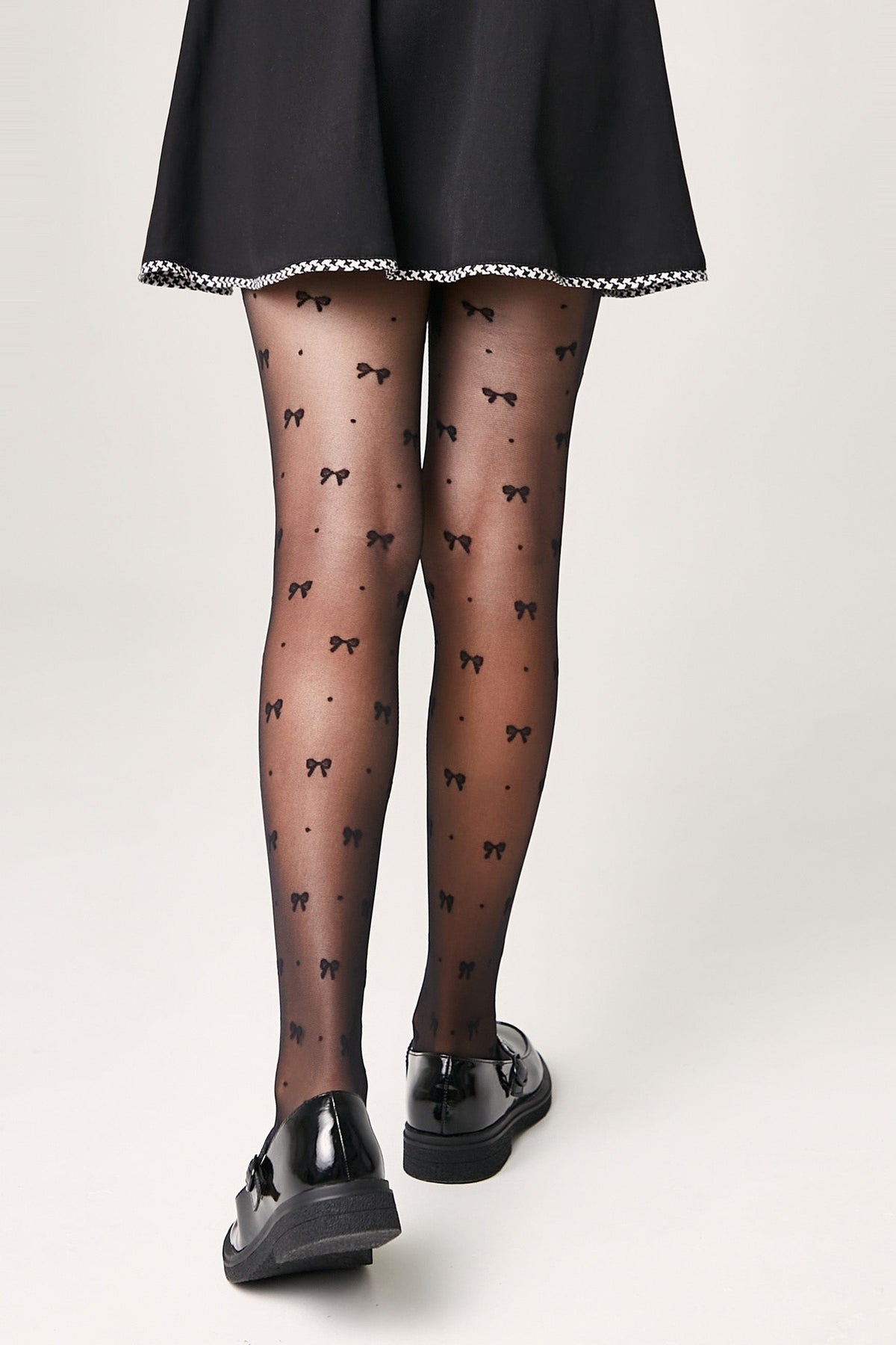 Sheer black tights decorated with a repeating pattern of small black bows, worn with a black skirt and black patent leather loafers.