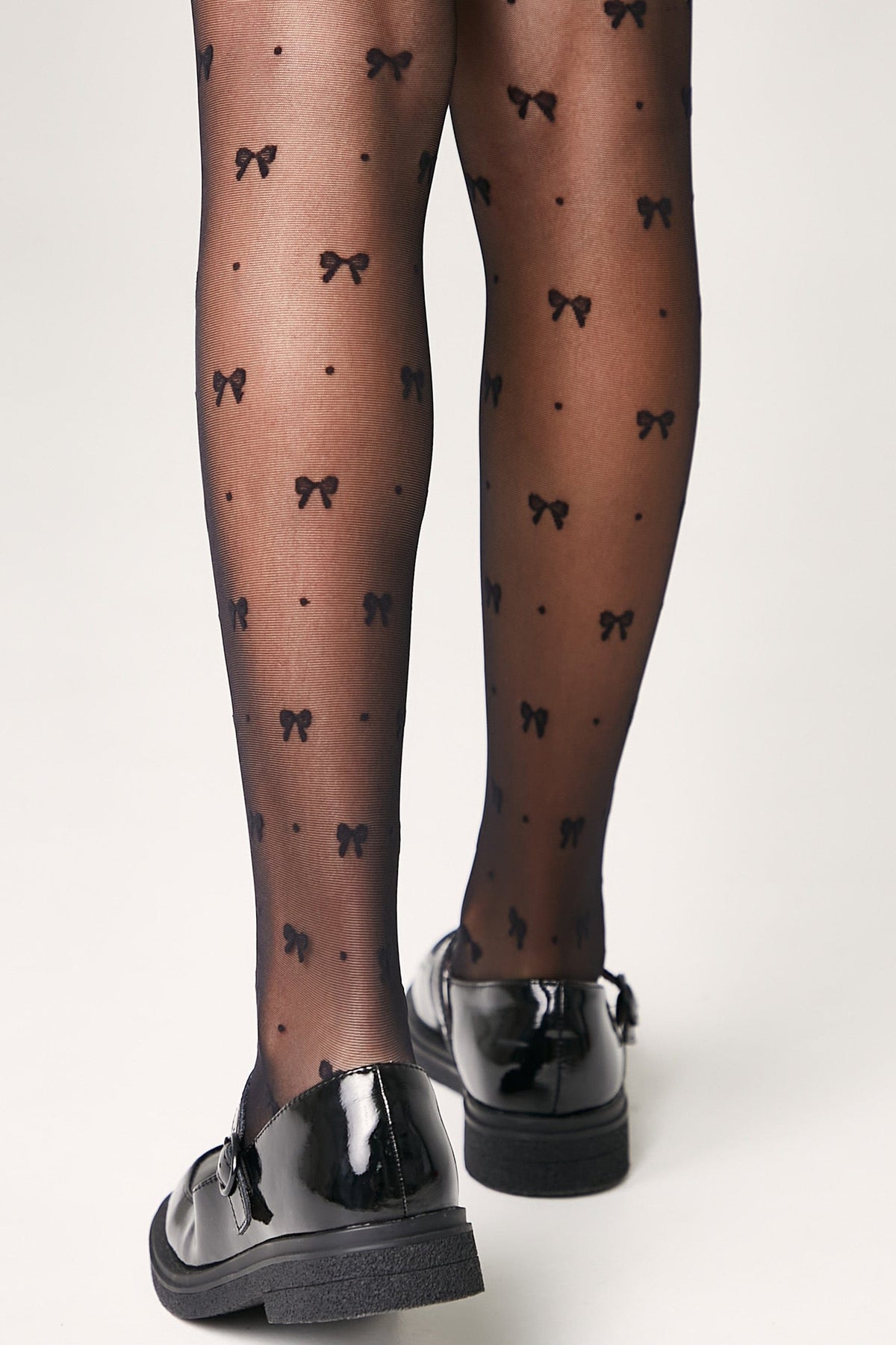Black sheer pantyhose featuring a repeating pattern of small bows and dots, paired with black patent leather Mary Jane shoes.