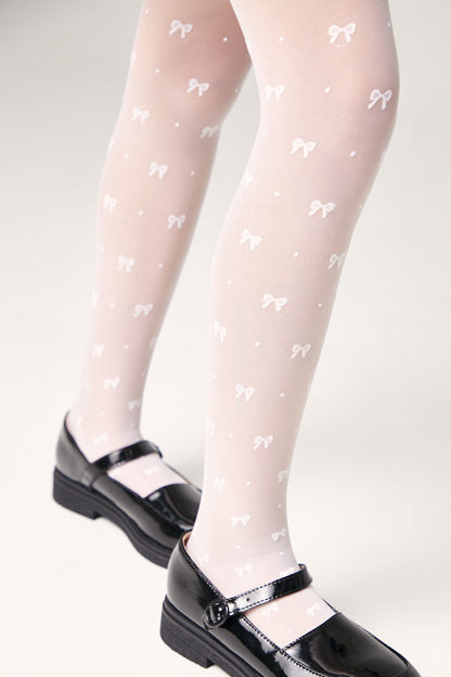 Sheer white tights decorated with a repeating pattern of small bows and dots, worn with black patent leather Mary Jane shoes.