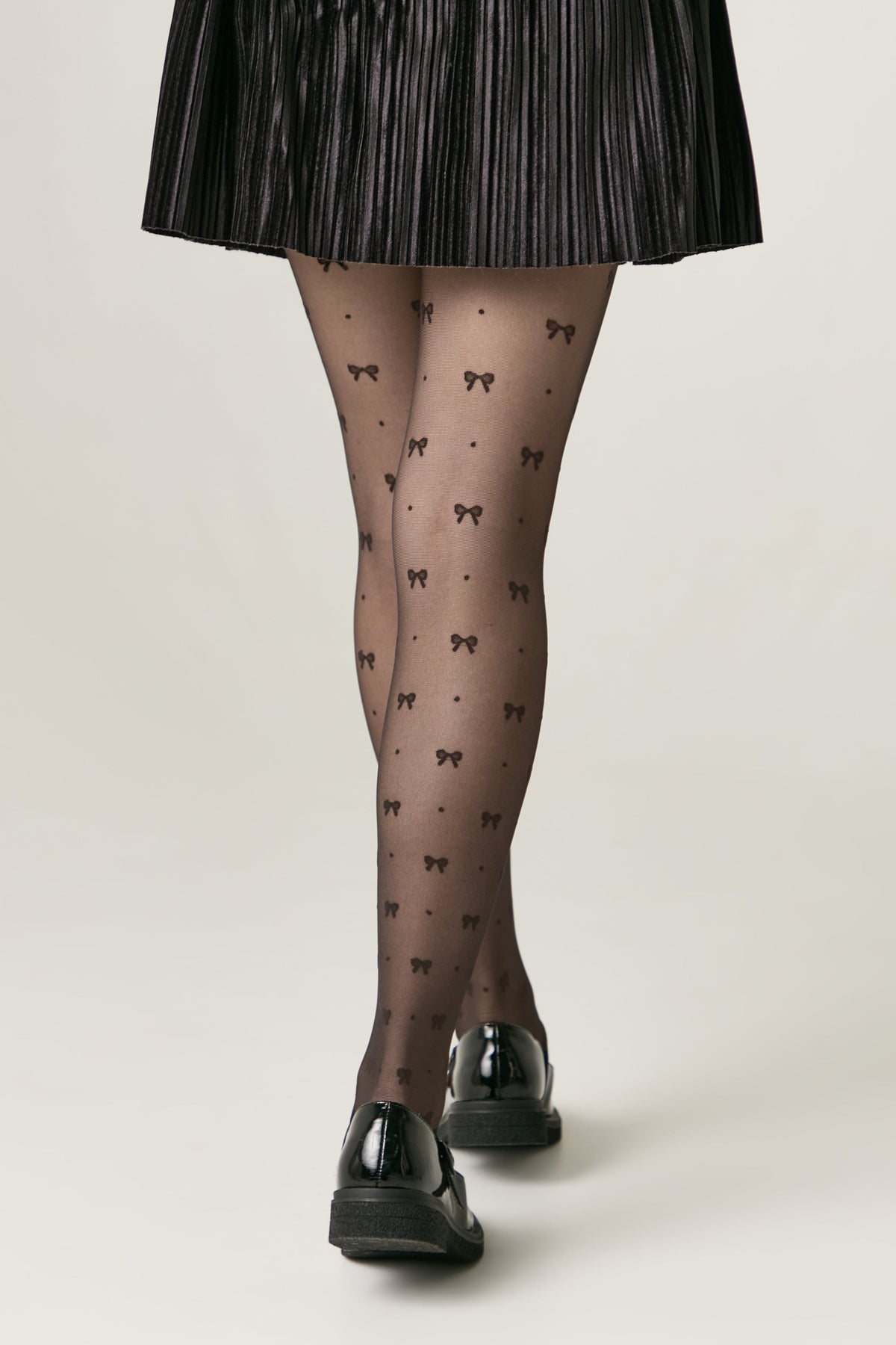 Sheer black tights featuring a repeating pattern of small bows and dots, worn with a pleated black skirt and black loafers.