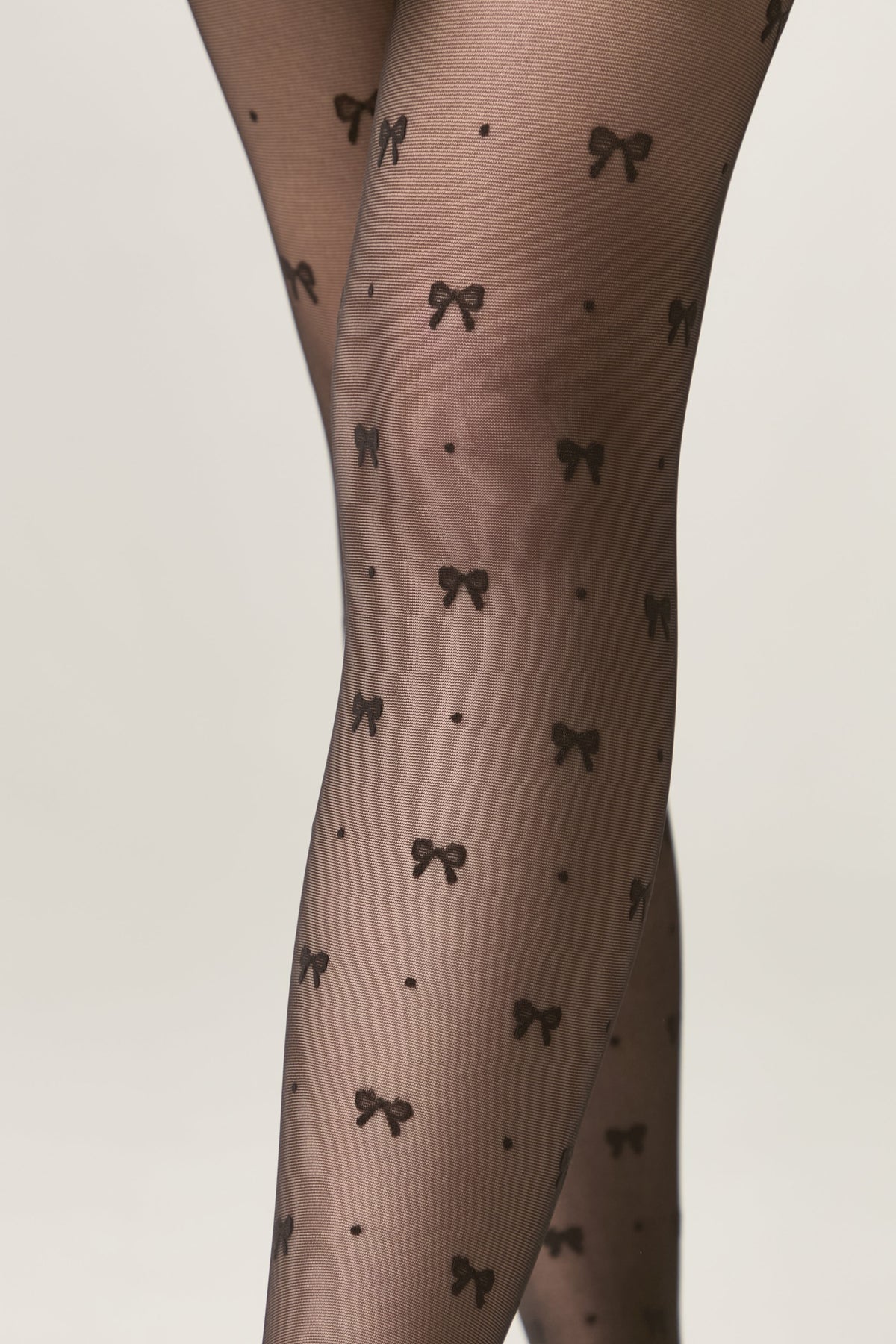 Sheer black tights feature a repeating pattern of small black bows and tiny dots against a light grey background.