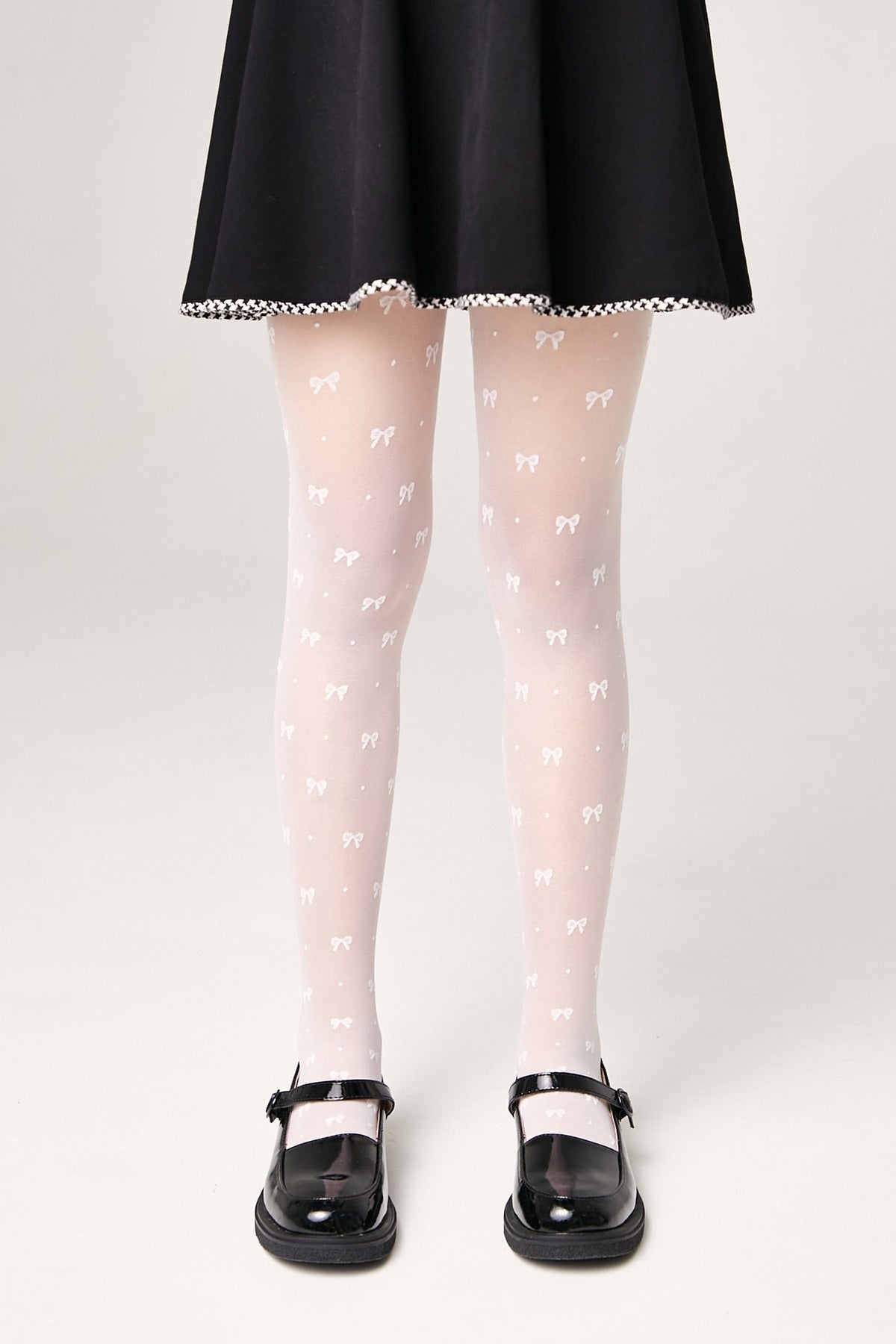 Sheer white tights featuring a repeating pattern of small bows and dots, paired with a black skirt and glossy black Mary Jane shoes.