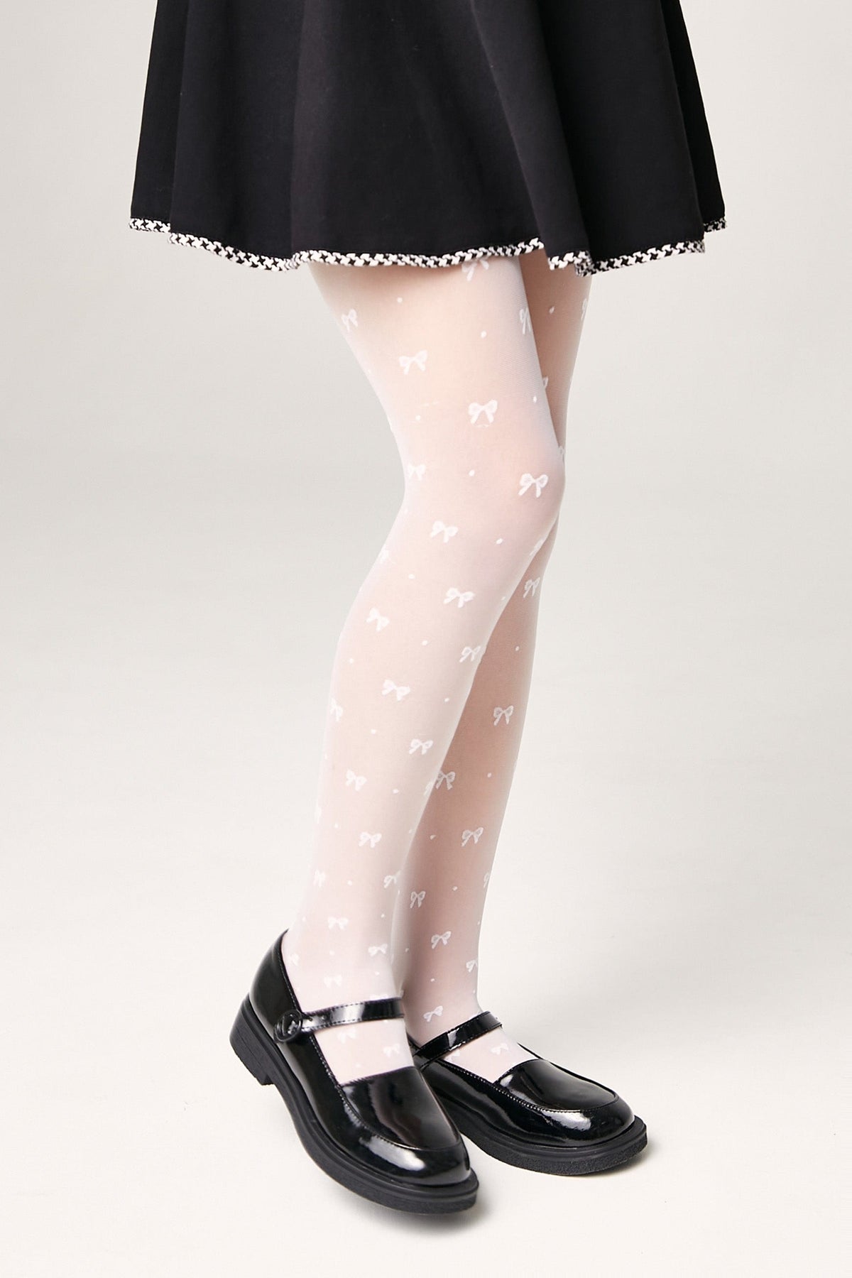 White sheer tights decorated with a small repeated bow pattern, worn with a black skirt and black mary jane shoes.
