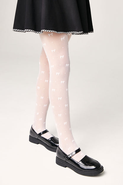 A person wears sheer white tights featuring a repeating pattern of small bows paired with black patent leather Mary Jane shoes and a black skirt.