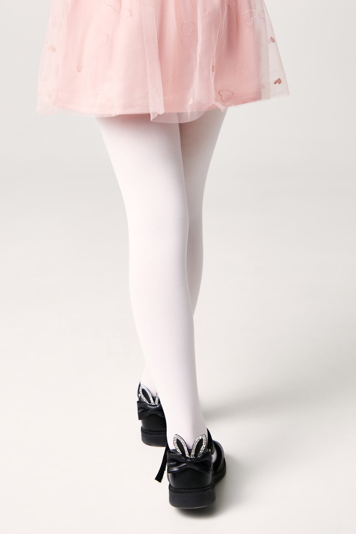 White tights worn with a pink skirt and black shoes decorated with rabbit ears and rhinestones.
