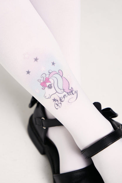 White tights featuring a pastel unicorn graphic with a bow, star motifs, and the word Beauty printed on the calf, paired with black buckled shoes.