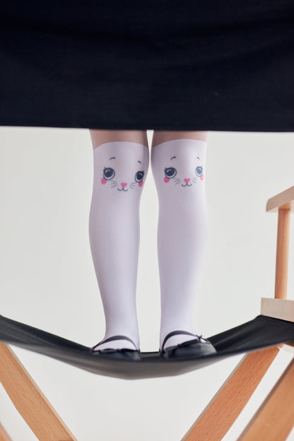 White knee-high socks with a cute cat face print on each knee, worn with black ballet flats while standing on a wooden director chair.
