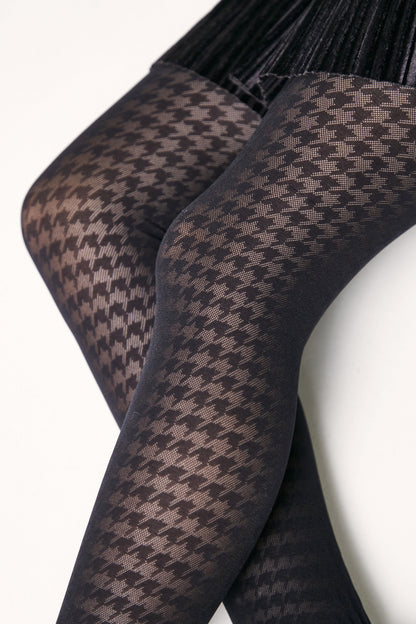 A person wears black sheer tights featuring an intricate houndstooth pattern paired with a black velvet skirt.