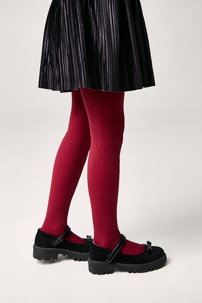 A pair of red patterned tights with a floral-like design, worn with black pleated skirt and black buckled mary jane shoes.