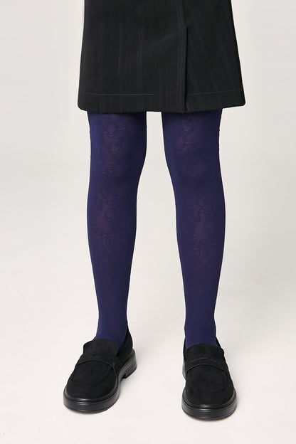 A person wears deep purple tights with an intricate tonal swirl pattern paired with a black skirt and black suede-like loafers.