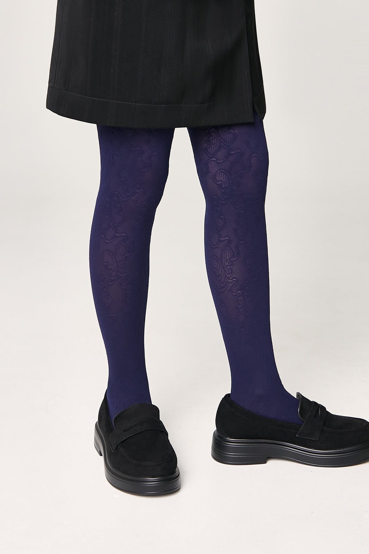 Dark purple patterned tights worn with black suede-style loafers and a black skirt.