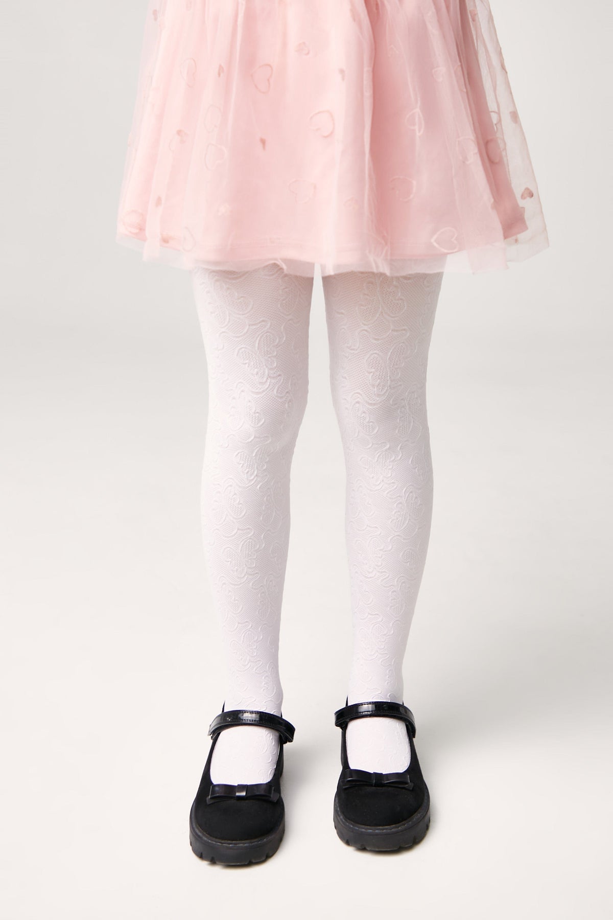 A pair of white tights with an embossed paisley pattern worn with black Mary Jane shoes and a pale pink tulle skirt with a heart print.