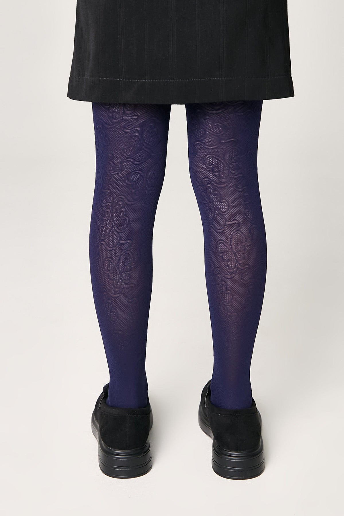 Dark purple patterned tights worn with a black skirt and black shoes against a plain white background.