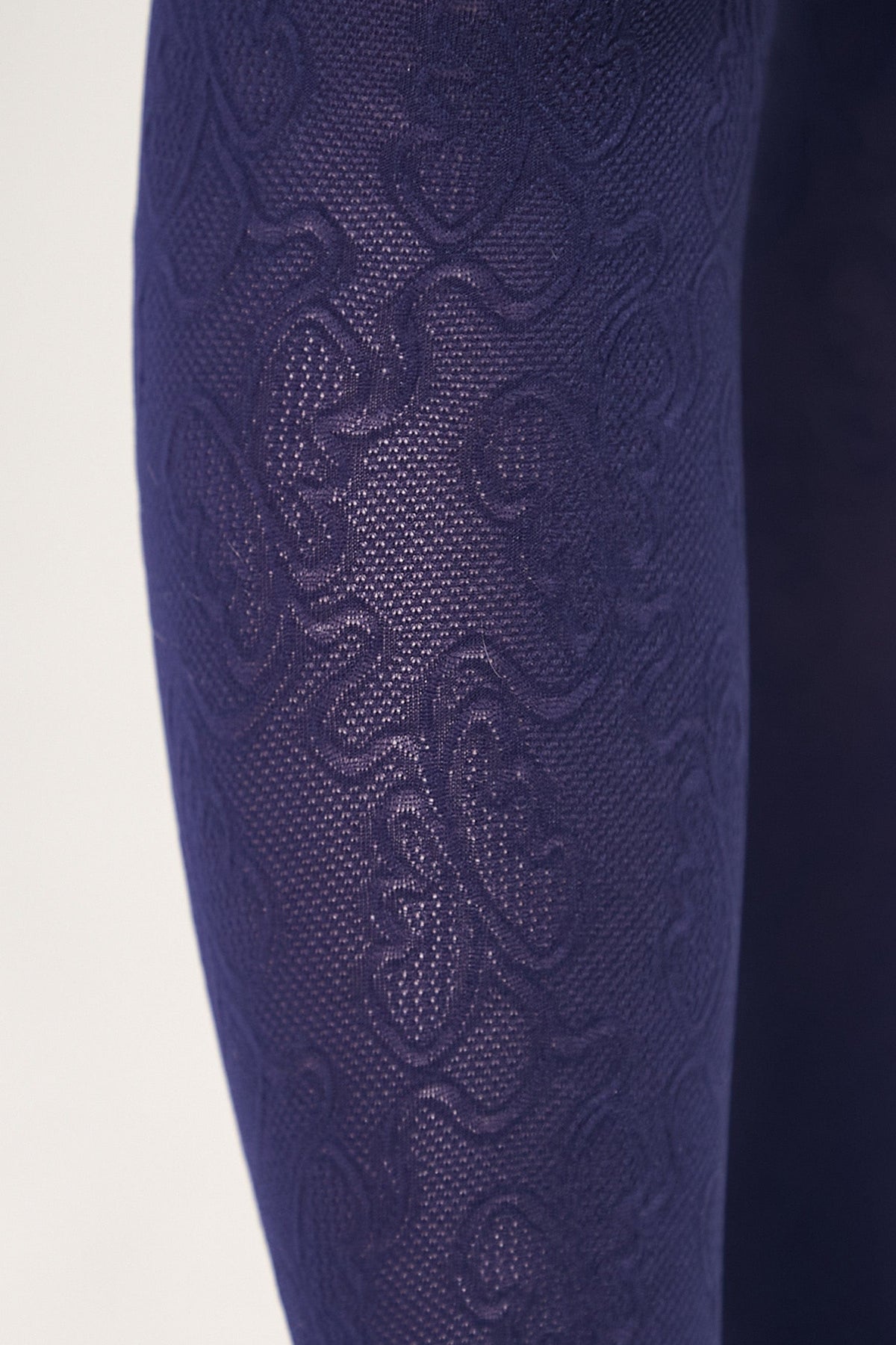 A close-up view of dark purple tights featuring a textured, raised floral pattern woven into the fabric.