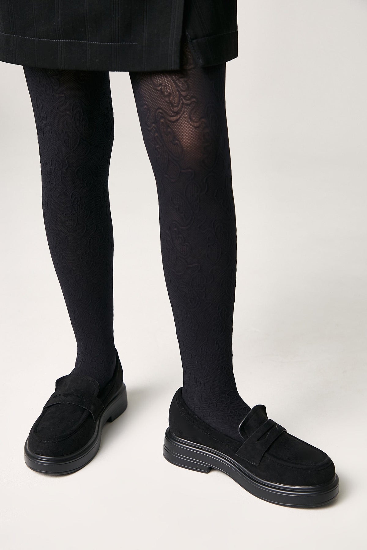Black loafers with thick rubber soles paired with dark, patterned tights and a black skirt.